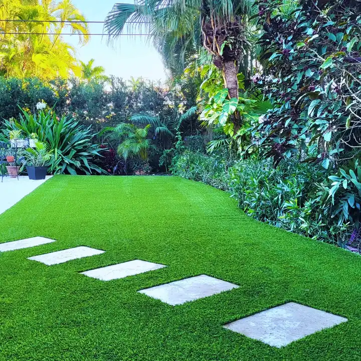 Artificial turf lawn with square stone stepping pads beside a tropical planting bed in a Hollywood Beach, Florida backyard