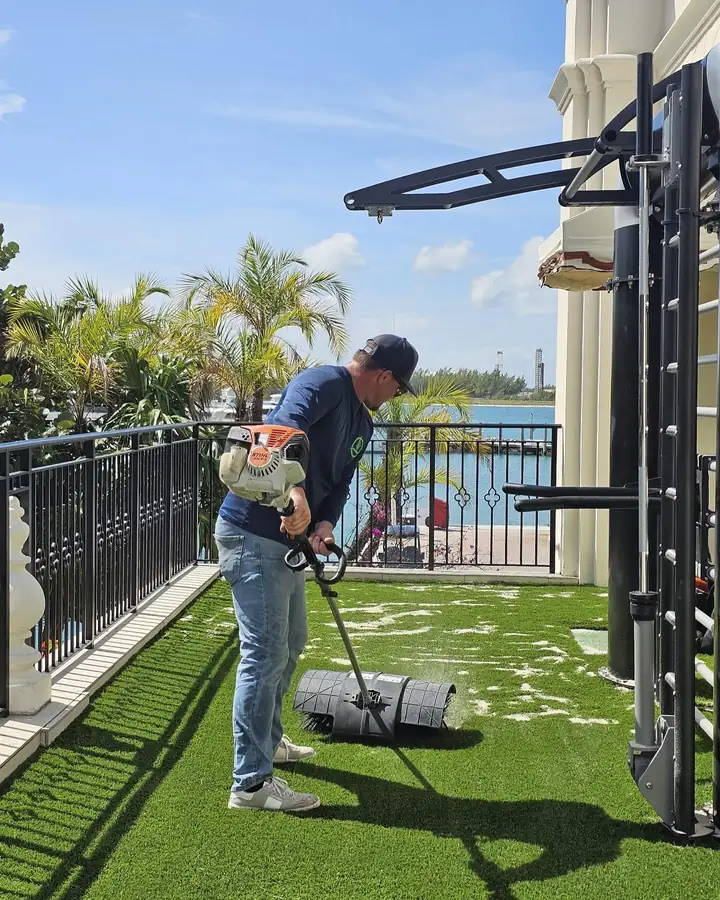 Installer power-brooming infill into new artificial turf beside outdoor gym equipment on a waterfront terrace in Miami, Florida