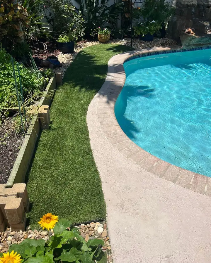Strip of artificial turf between a curved pool deck and a raised planter in a Boca Point backyard