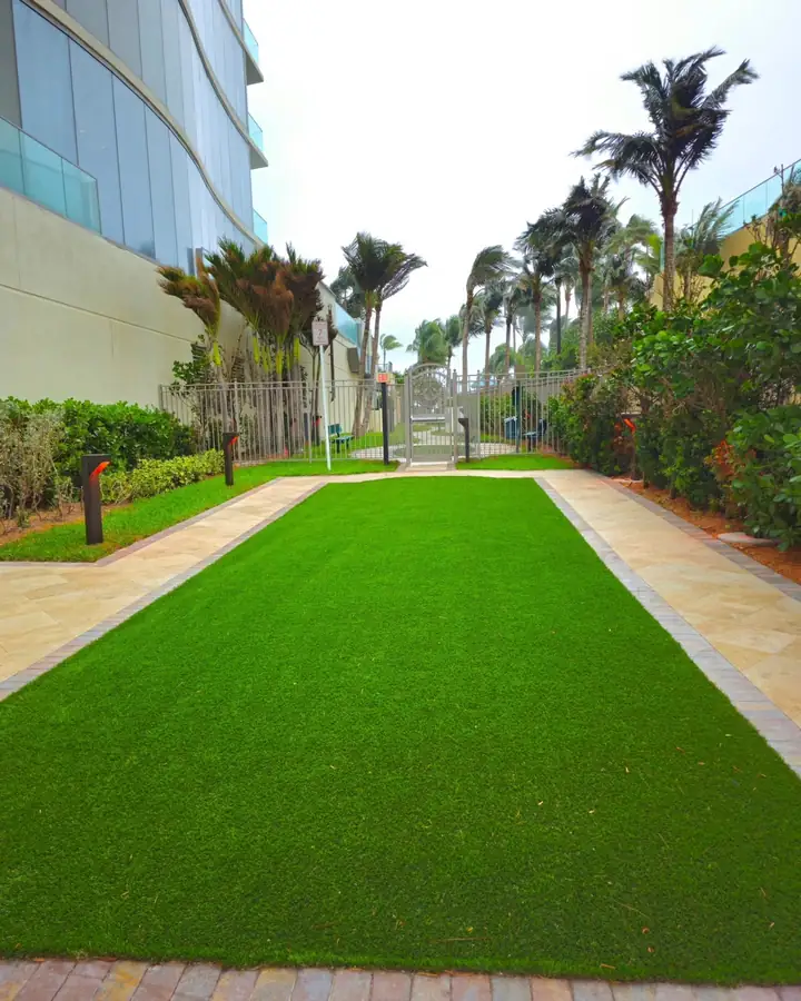 Rectangle of artificial turf framed by travertine walkways and a paver band beside a high-rise hotel in Sunny Isles Beach, Florida