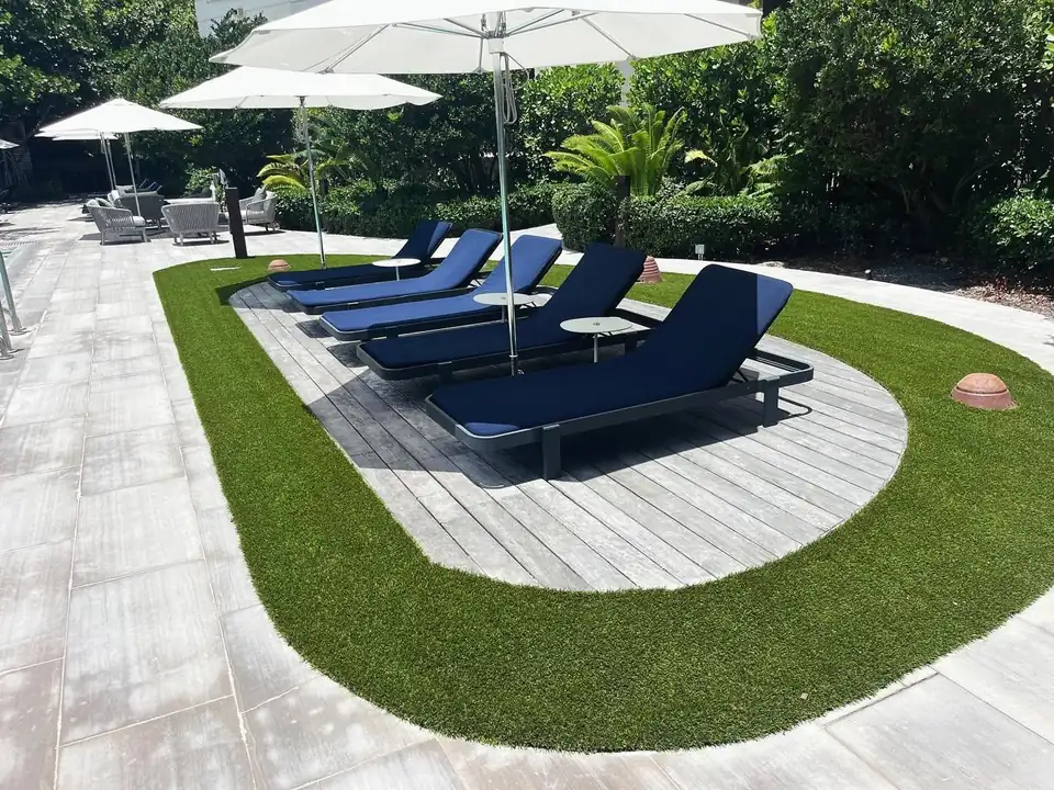 Artificial turf bordering an oval lounge deck with blue chaise lounges and white umbrellas at a Boca Point pool area